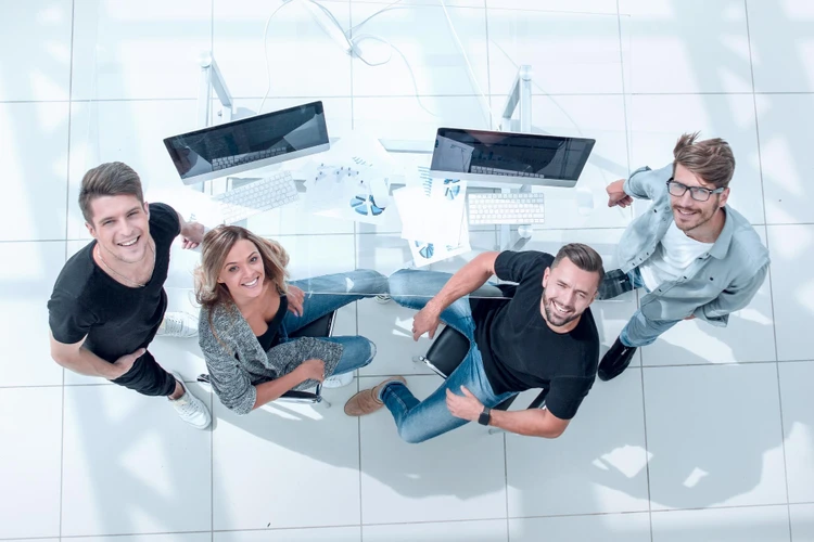 Four smiling people around a desk with computers and papers, looking up at the camera.