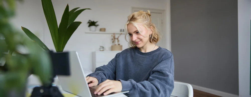 Young woman in a gray sweater typing on a laptop at home.